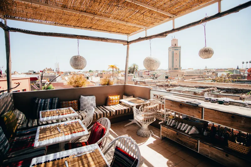 Shaded rooftop terrace with woven lamps above a medina, a minaret in the distance