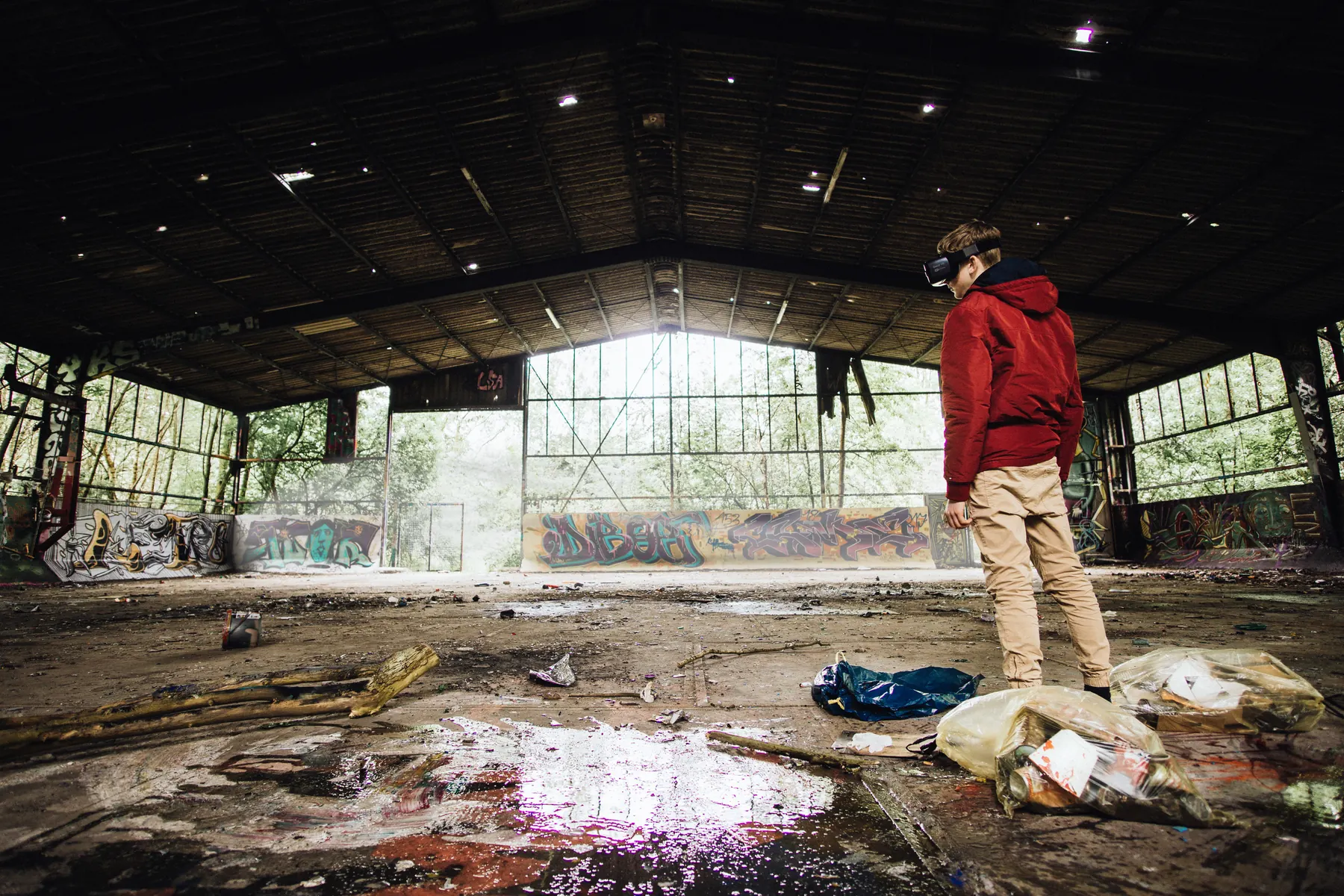 Empty hall with a rusted roof and graffiti walls, wet floor catching the light