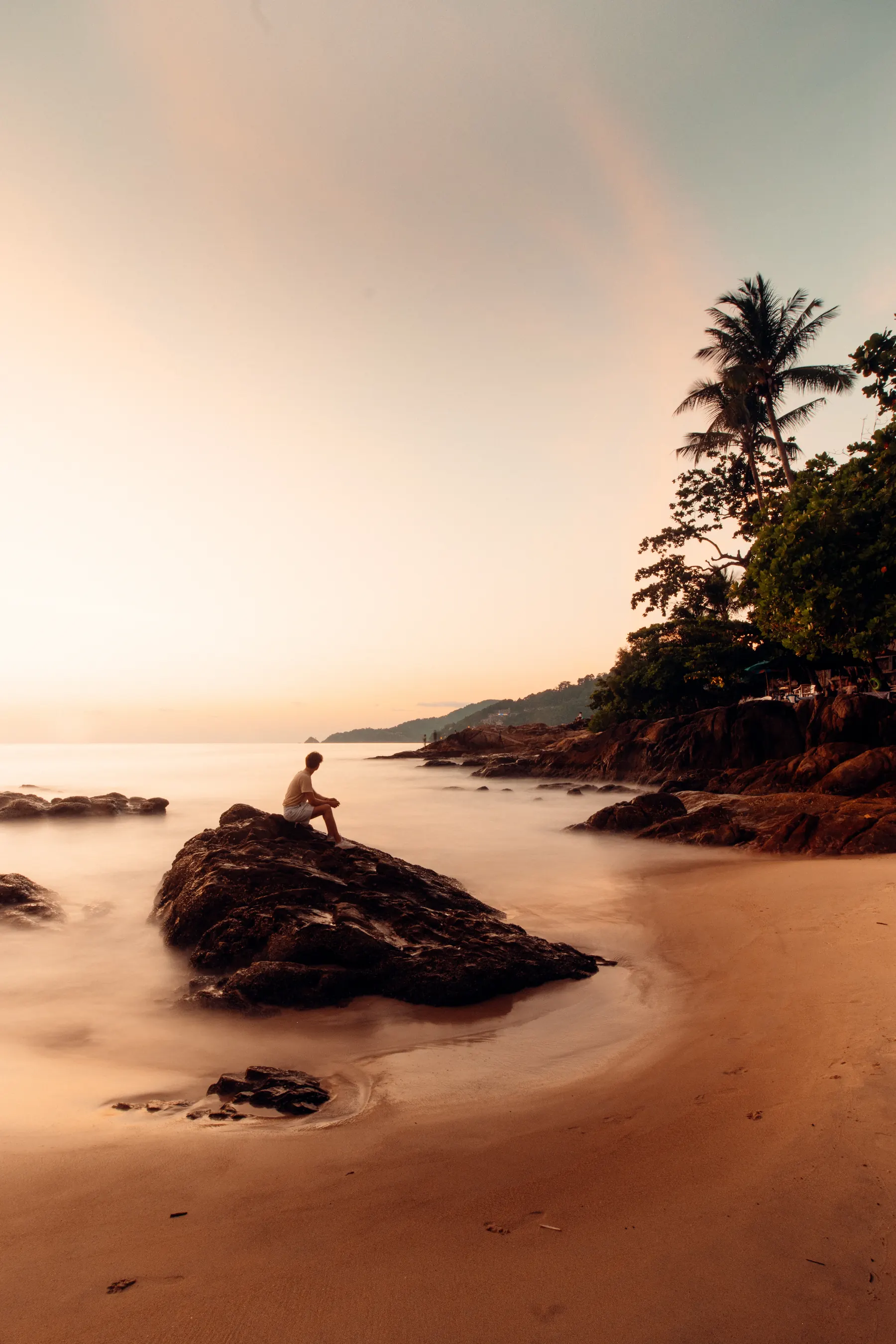 Tide blurred to mist around a rock, palms on the headland at sunset