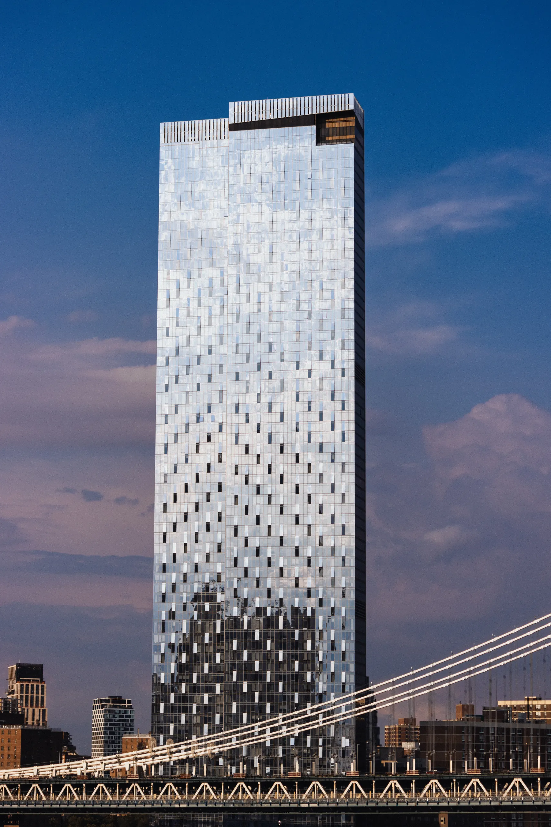 Glass tower catching the afternoon light behind the cables of a suspension bridge